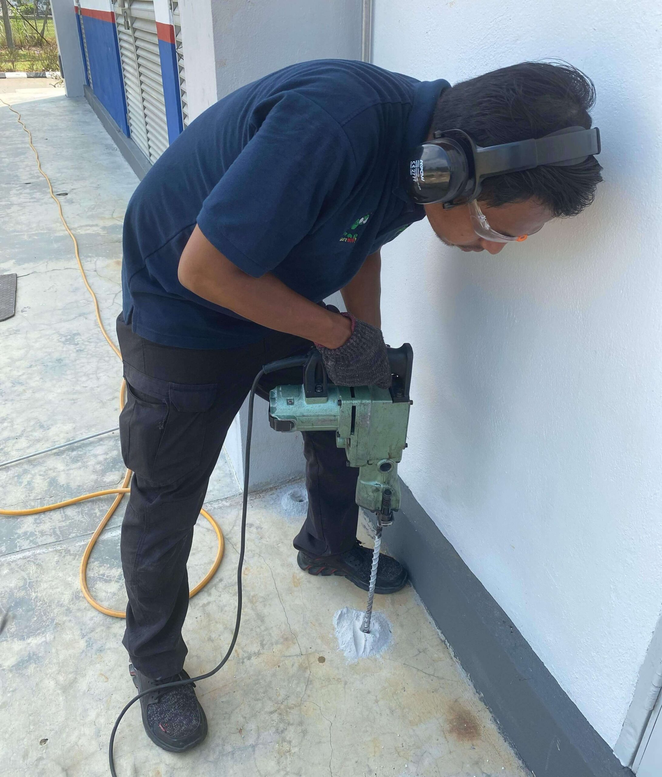 A man is drilling the floor for corrective soil treatment during termite pest control treatment services.